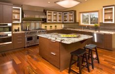 a large kitchen with wooden floors and stainless steel appliances, including an island in the center