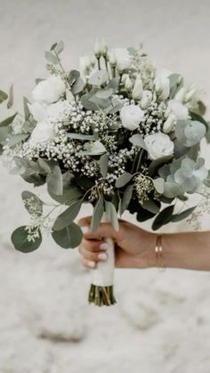 a person holding a bouquet of flowers in their hand on the beach with sand behind them