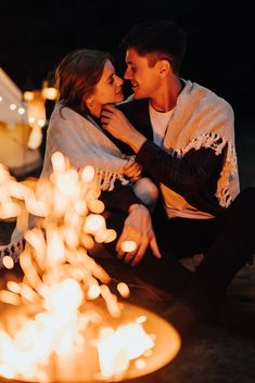 a man and woman sitting next to a fire pit with their arms around each other