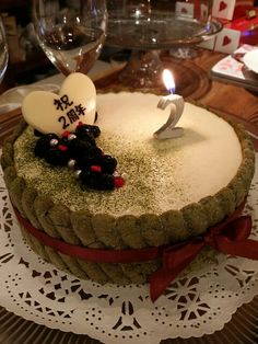 a cake with two candles on top of it sitting on a doily next to wine glasses