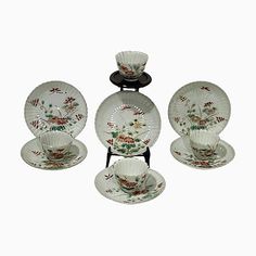 an assortment of china plates and cups on display against a white background, including one with red flowers