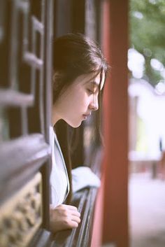 a woman is sitting on a bench looking down at her cell phone while she looks out the window