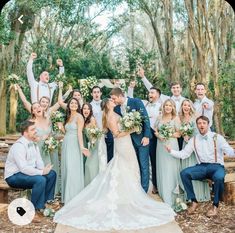 a large group of people standing around each other in front of some trees and bushes