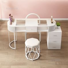 a white desk with two drawers and a stool next to it on the floor in front of a pink wall