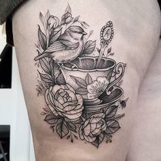 a bird sitting on top of a teacup with roses around it and a spoon in the cup