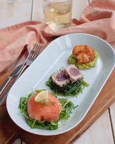 a white plate topped with food next to a fork and glass of wine on top of a wooden table