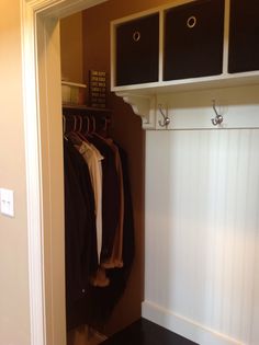 an open closet with clothes hanging on hangers and two black bins next to it