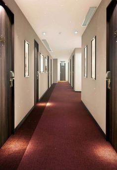 a long hallway with red carpeting and two doors leading to another room that has pictures on the walls