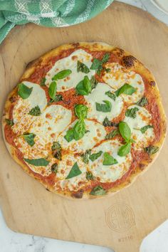 a pizza sitting on top of a wooden cutting board next to a green towel and knife