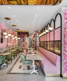 the interior of a fancy restaurant with pink flowers on the walls and green velvet chairs