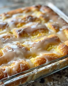 a glass dish filled with cinnamon rolls covered in icing and glaze on top of a granite counter