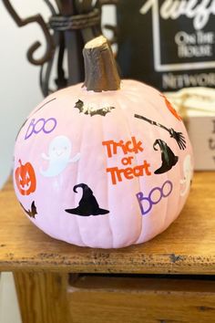 a pink pumpkin with halloween stickers on it sitting on top of a wooden table