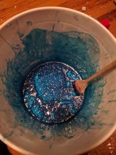 a wooden spoon in a blue mixing bowl filled with liquid and water on top of a wood table