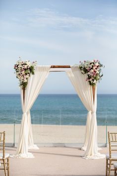 an outdoor wedding ceremony setup with white drapes and flowers on the altar, overlooking the ocean