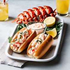 two lobster sandwiches on buns with dipping sauce and lemon wedges next to them