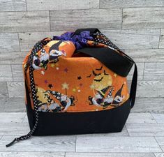 an orange halloween bag with black trim and witches on it, sitting on a wooden floor