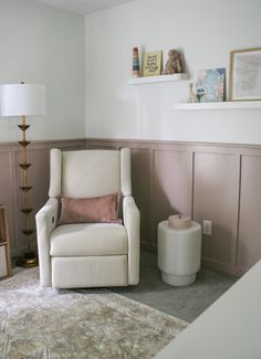 Nursery glider and side table in a small room. Cute organization of floating shelves on the walls, side table next to the glider, and cube storages for books and toys. White walls with pink board and batten. Small Nursery Ideas Panelling, Nursery With Built In Bookshelves, Nursery Wall Board And Batten, Panelling Walls Nursery, Baton Board Wall Nursery, Dado Rail Nursery Pink, Light Pink Board And Batten, Shelves Above Board And Batten, Blush Wainscoting