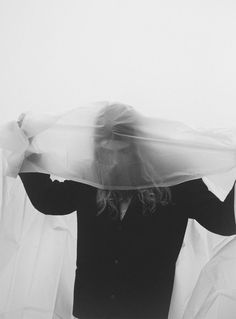 a woman covering her face with a veil in front of her head while standing under white sheets