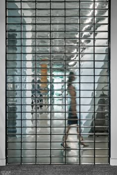 the reflection of a man riding a skateboard through a metal gate in an office building