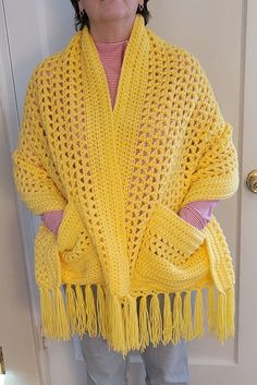 a woman standing in front of a door wearing a yellow crocheted shawl