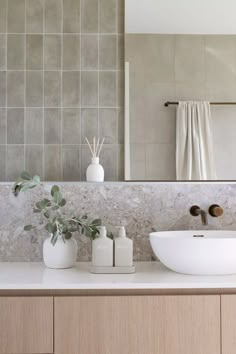 a bathroom sink sitting under a large mirror next to a white vase with leaves on it