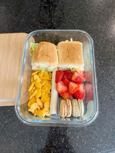 a plastic container filled with sandwiches, fruit and crackers next to a cutting board