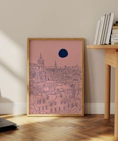 a pink and blue cityscape is framed in a wooden frame on the floor