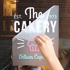 a person holding up a sign in front of a store window that says the bakery