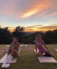 two women sitting on yoga mats in front of the sunset with their arms crossed and legs crossed