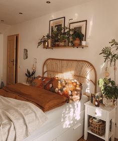 a bed sitting in a bedroom next to two plants on top of a white table