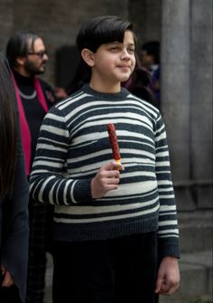 a young boy holding an object in his hand while standing next to other people on the sidewalk