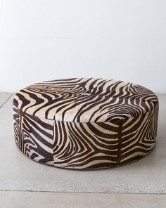 a zebra print ottoman sitting on top of a cement floor next to a white wall