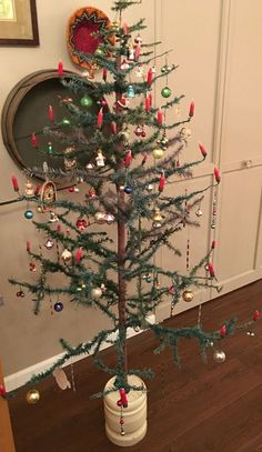 a small christmas tree with ornaments on it in front of a wall and wooden floor