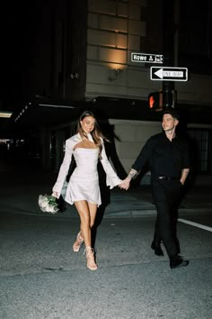 a man and woman holding hands as they walk down the street in front of a traffic light