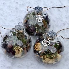 three ornaments are sitting in the snow on top of each other, one is filled with plants