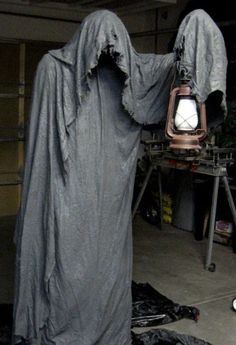 a creepy looking statue with a lantern in it's hand and some sort of cloth on the ground