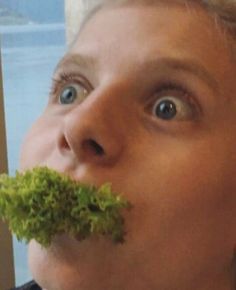 a young man is eating some lettuce in front of his face