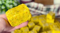 a hand holding up a piece of food in front of a pile of yellow cubes