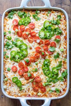 a casserole dish with tomatoes, green peppers and cheese in it on a wooden table