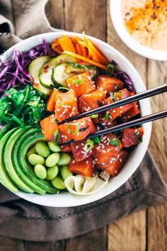 a bowl filled with vegetables and chopsticks on top of a wooden table