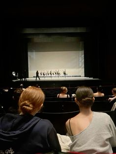 some people are sitting in front of an empty stage and watching something on the screen