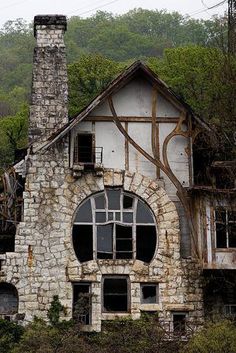 an old stone building with windows and vines growing on the roof, in front of mountains