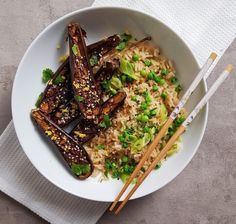 a white bowl filled with rice, vegetables and chopsticks on top of a table