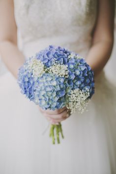 a bride holding a bouquet of blue and white hydrangeas on her wedding day