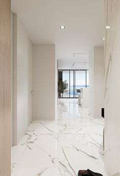 an empty hallway with marble flooring and white walls, leading to the balcony overlooking the ocean