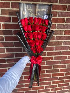 someone is holding a bouquet of roses in front of a brick wall with writing on it