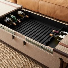 an open suitcase filled with wine bottles on top of a carpeted floor next to a couch