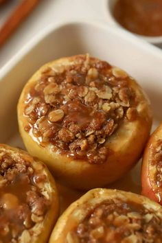 baked apples in a white dish with cinnamon toppings on top and two bowls of dipping sauce behind them