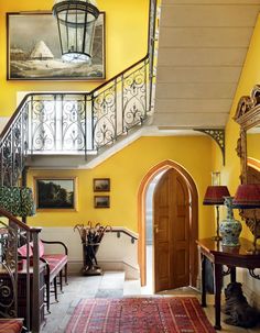 an entry way with yellow walls and ornate iron railings is flanked by a red rug on the floor