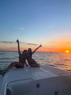 two women sitting on the back of a boat at sunset